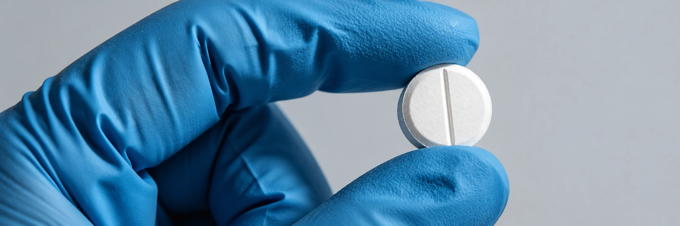 A gloved hand holding a scored tablet